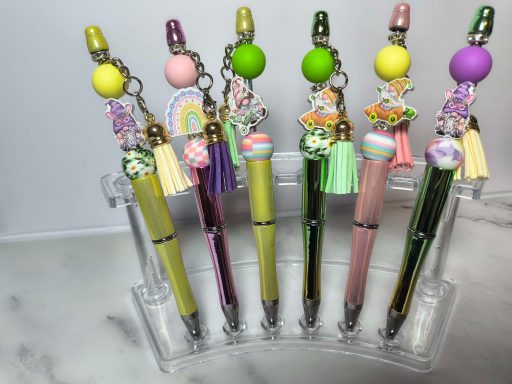 Colorful pens with decorative charms displayed in a clear holder.